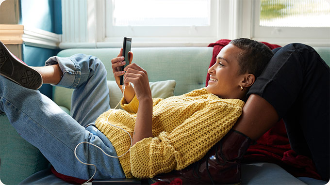 A person laying on a couch smiling looking at a cell phone.